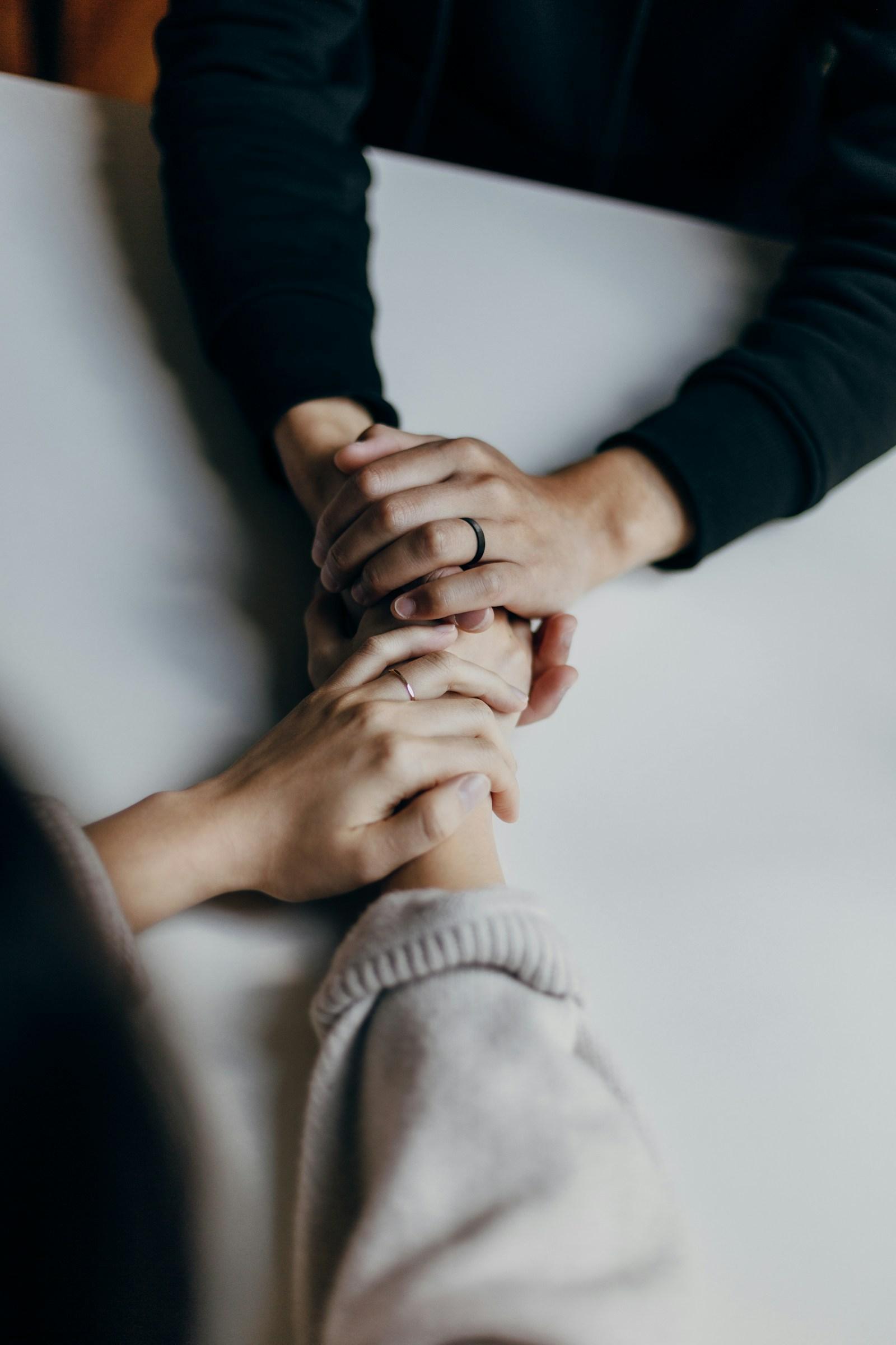 Two people holding hands across a table in a gesture of comfort